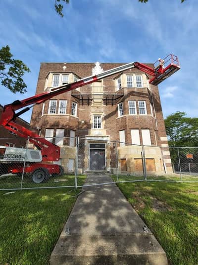 Multi-story brick building with a red aerial lift positioned against the facade.