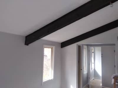 Interior room with exposed black beams and white walls with natural window light.