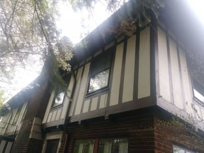 Dark siding house with white covered porch and mature landscaping.
