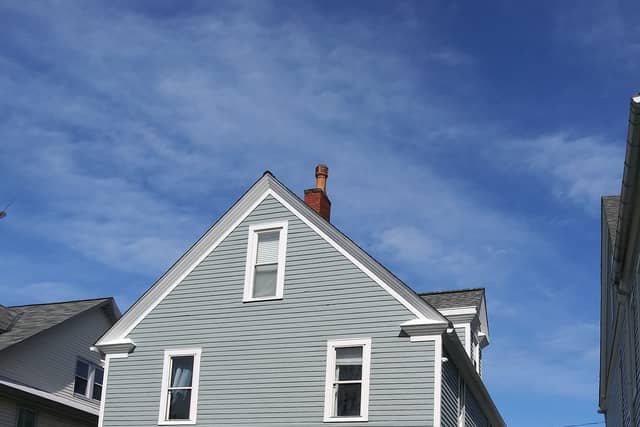 The same clapboard house finished in grey-blue with white trim and a red front door.