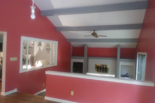 A room with a deep red accent wall, white trim and grey painted ceiling beams.
