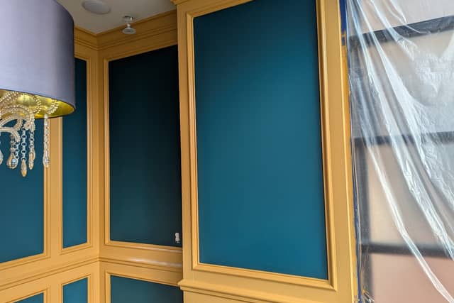 Teal wall panels framed in gold-painted moulding, with plastic sheeting still hanging.